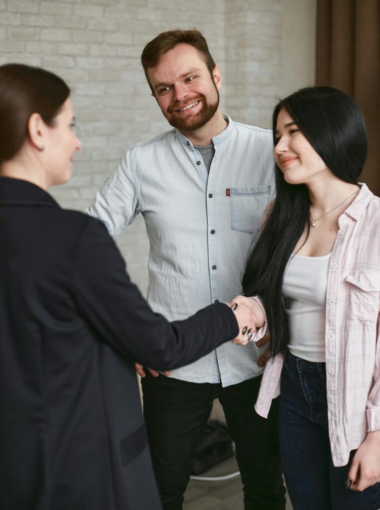 Three adults shaking hands in a professional meeting setting, showing agreement and positive interaction.